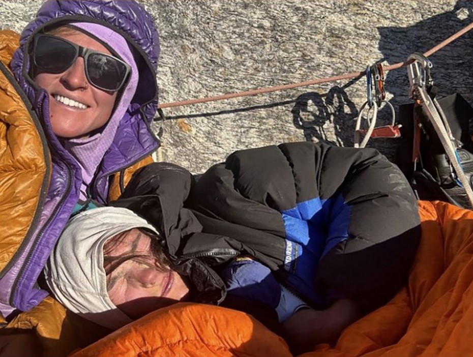 a woman wearing sunglasses is laying next to another woman in an orange sleeping bag