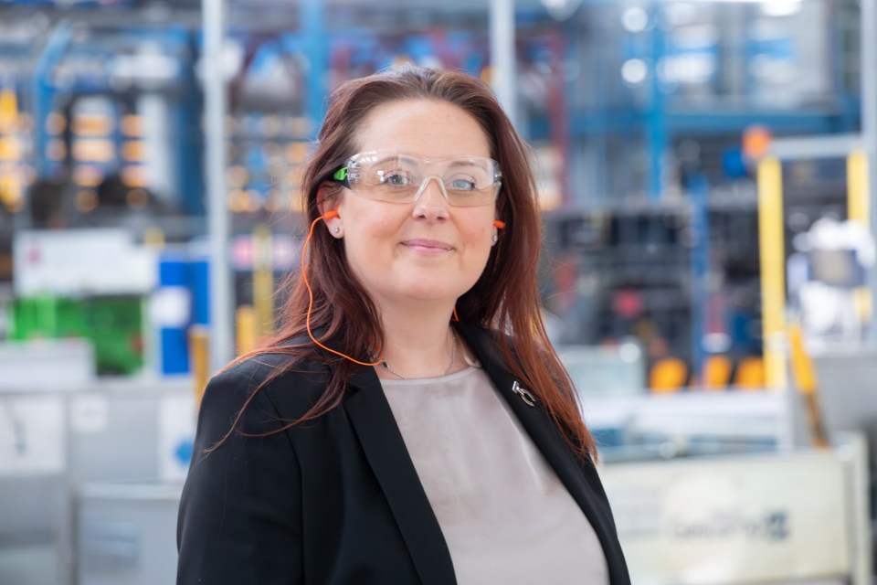 a woman wearing safety glasses and ear plugs smiles for the camera