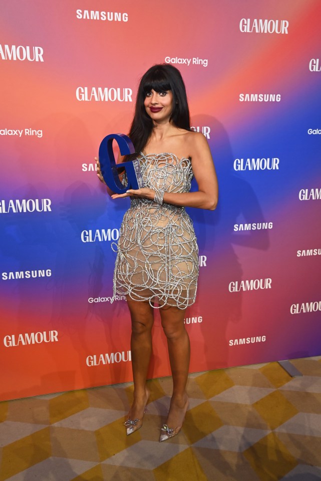 a woman holding an award in front of a wall that says glamour