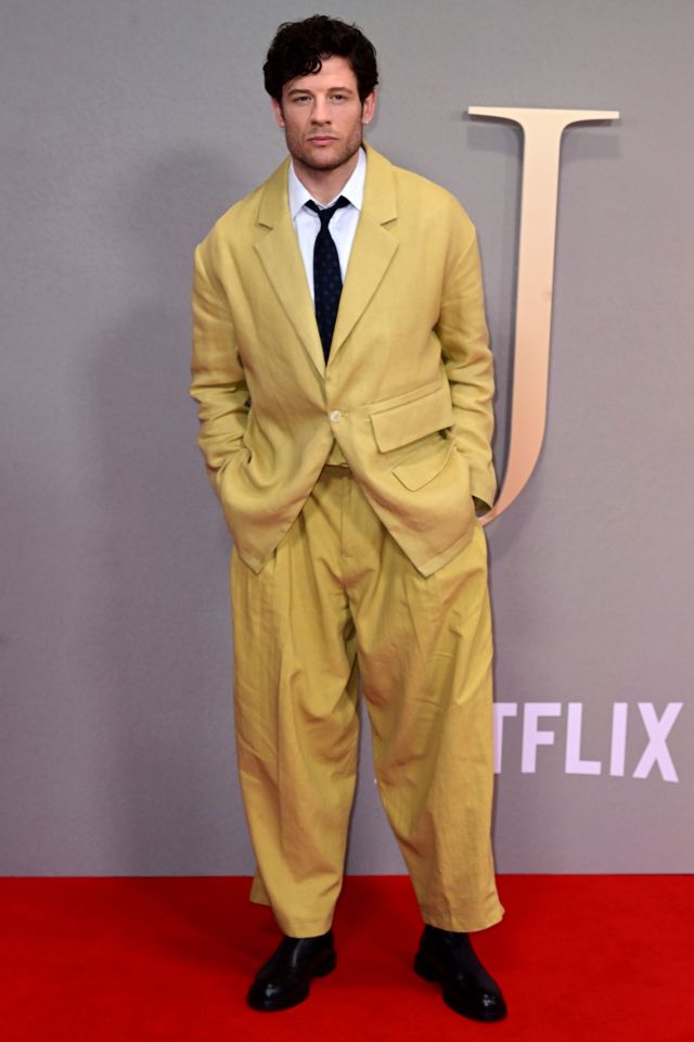 a man in a yellow suit stands on a red carpet in front of a sign that says netflix