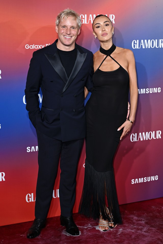 a man and woman pose on a red carpet that says glamour