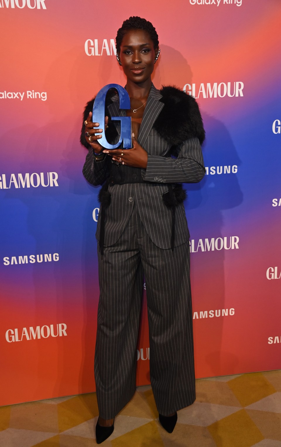 a woman in a suit is holding a large blue letter g