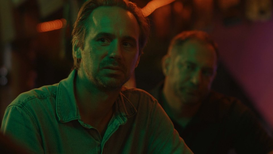 a man in a green shirt sits in a dark room