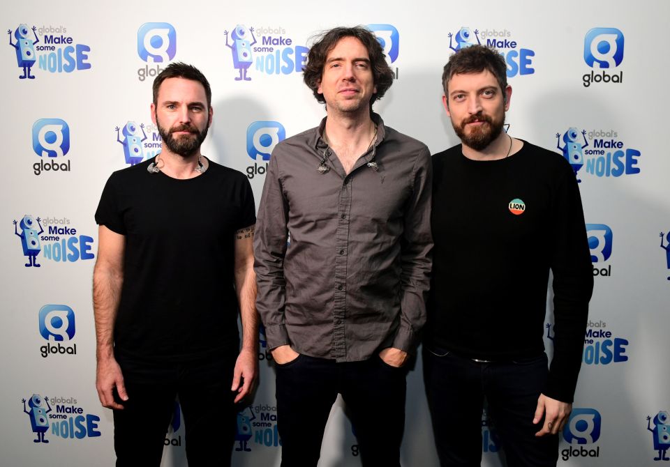 three men stand in front of a wall that says make some noise