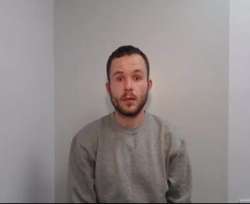 a man with a beard is sitting in front of a white wall .