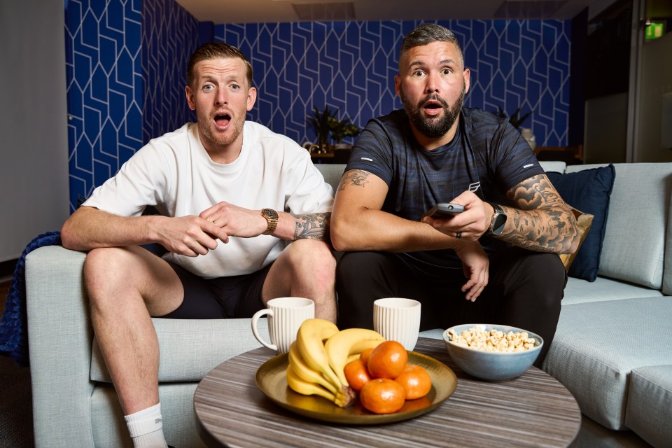 two men sitting on a couch with a bowl of popcorn