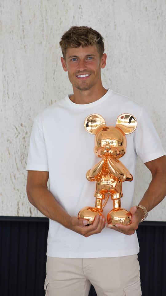 a man in a white shirt is holding a gold mickey mouse statue