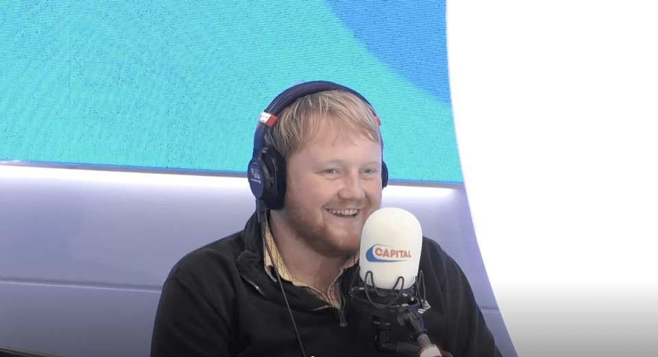 a man wearing headphones stands in front of a capital radio microphone