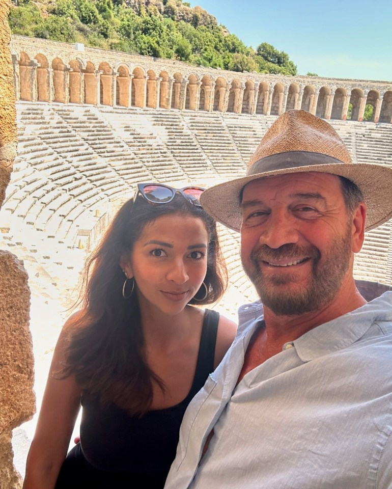 a man and a woman are posing for a picture in front of an amphitheater