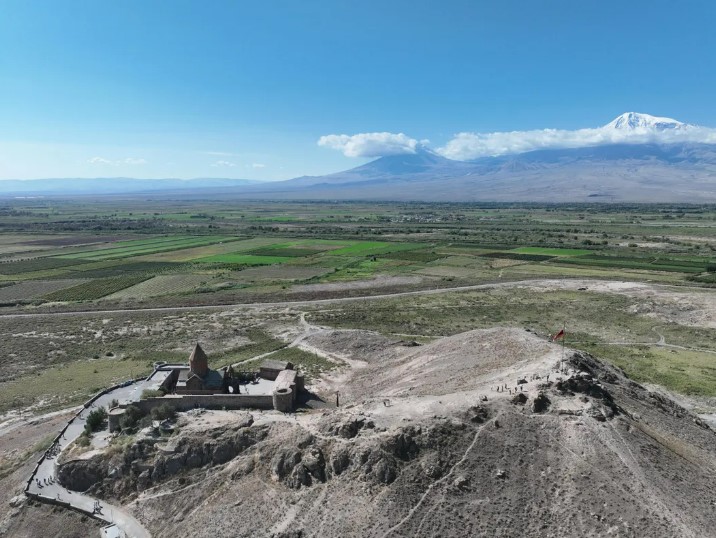 an aerial view of a church on top of a hill with mountains in the background