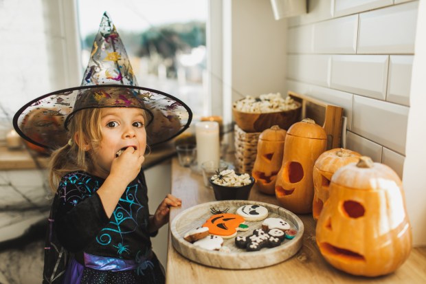 a little girl in a witch costume eating a cookie