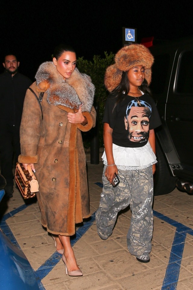 a woman in a fur coat stands next to a girl wearing a t-shirt with a picture of a man on it