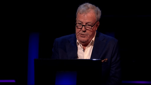 a man in a suit and glasses is sitting in front of a laptop computer on a stage .