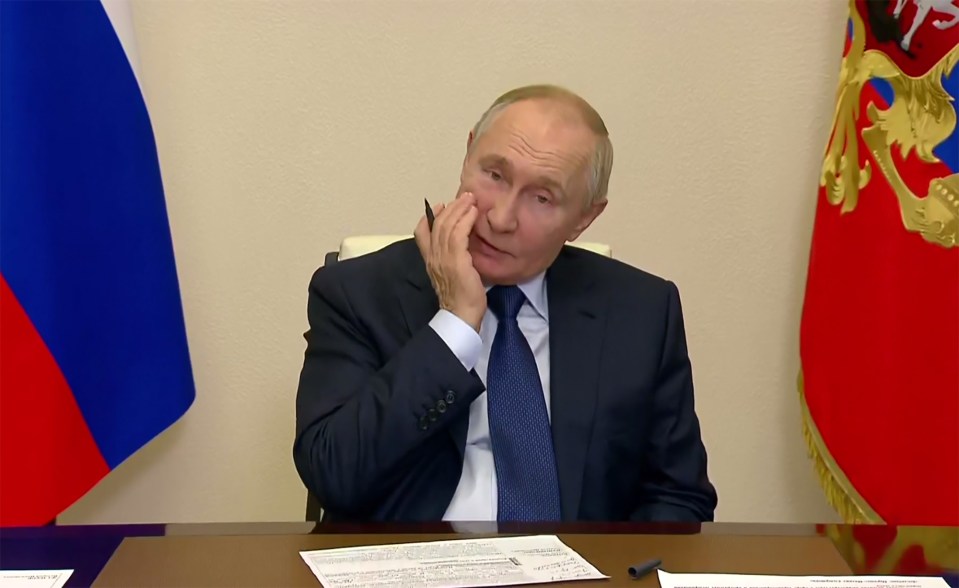 a man in a suit and tie sits at a desk in front of a russian flag