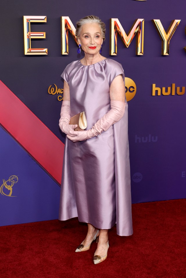 a woman in a purple dress and pink gloves is on the red carpet at the emmy awards