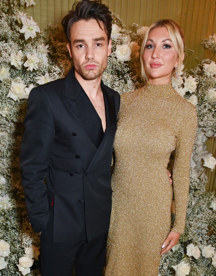 a man in a black suit stands next to a woman in a gold dress