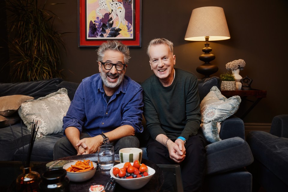 two men sit on a couch with a bowl of fruit on the table