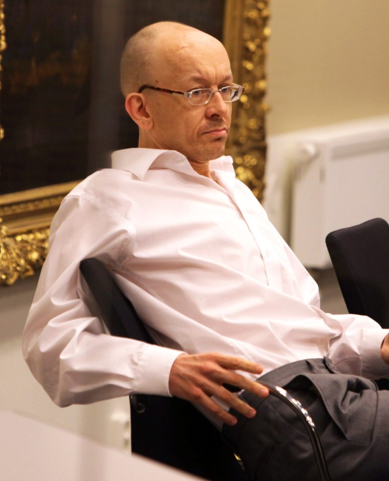 a bald man wearing glasses sits in a chair