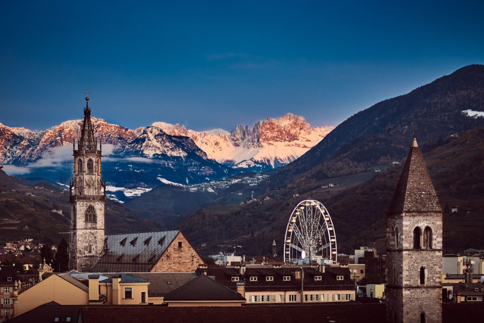 a ferris wheel is in the foreground of a city with mountains in the background