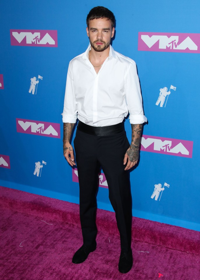 a man in a white shirt and black pants stands on a pink carpet in front of a blue wall that says vma