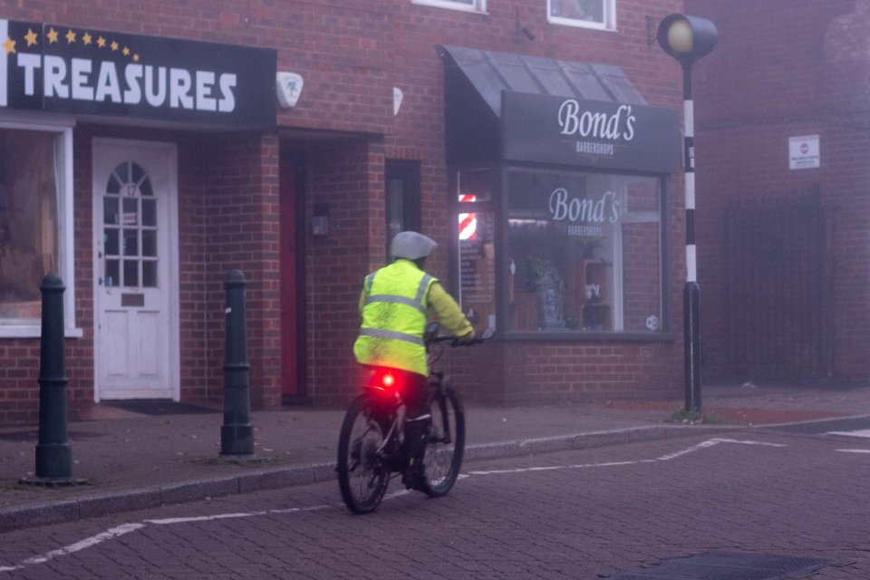 A cyclist wears a high viz jacket and has their lights on first thing today in Fordingbridge, New Forest, Hampshire