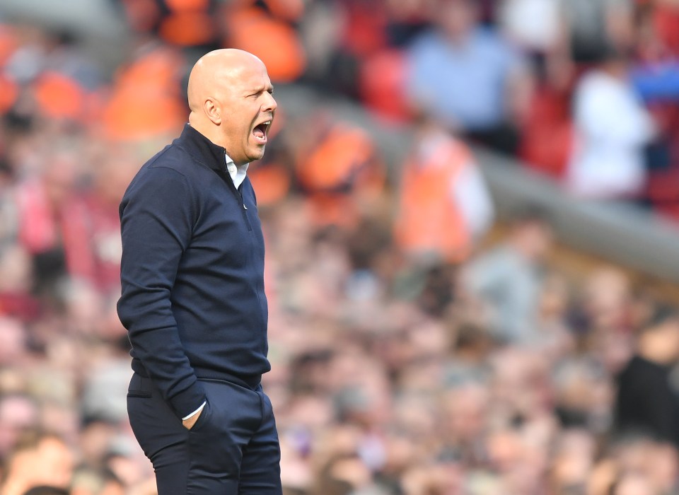 a bald man in a blue sweater is shouting in front of a crowd