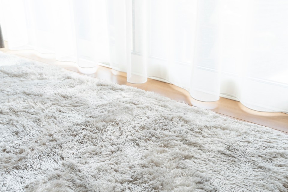 a white rug sits in front of a window with white curtains