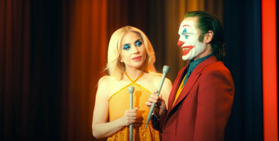 a man in a clown costume stands next to a woman in a yellow dress