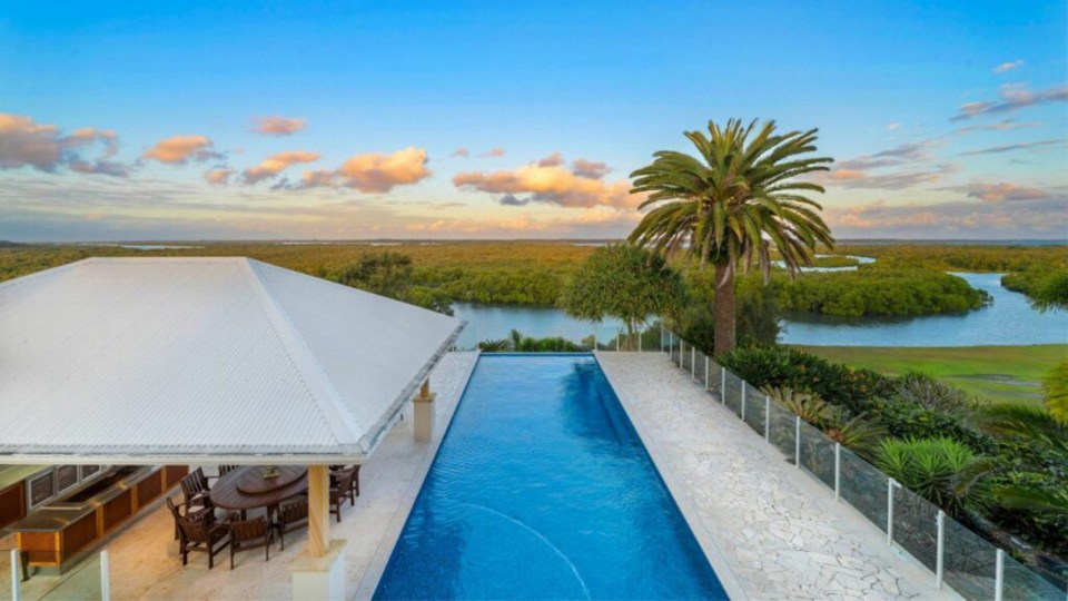 a large swimming pool with a table and chairs surrounded by palm trees