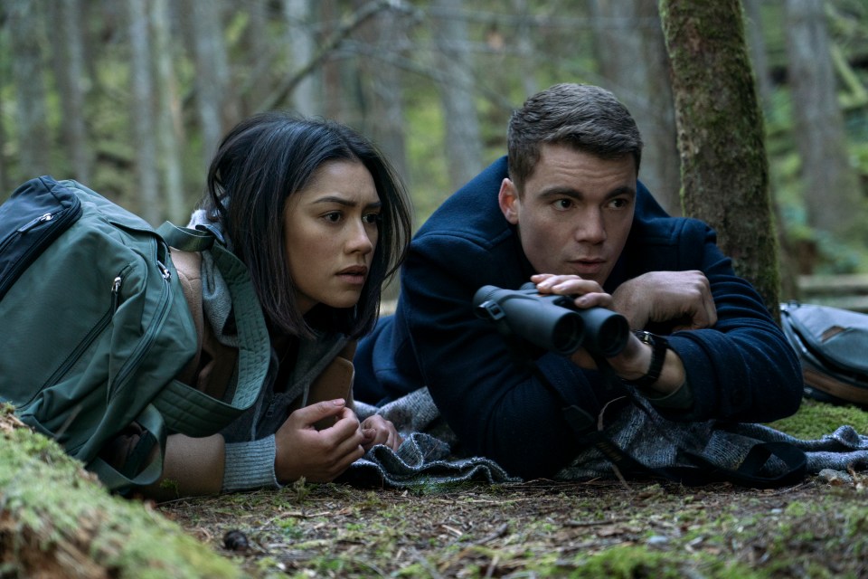 a man and a woman are looking through binoculars in the woods