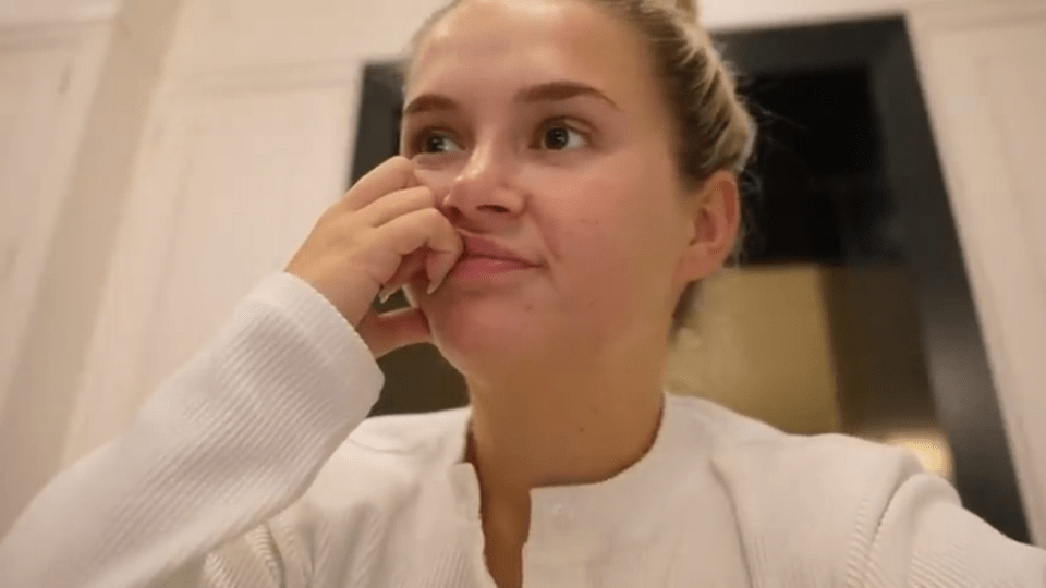 a woman in a white shirt wipes her nose with her hand