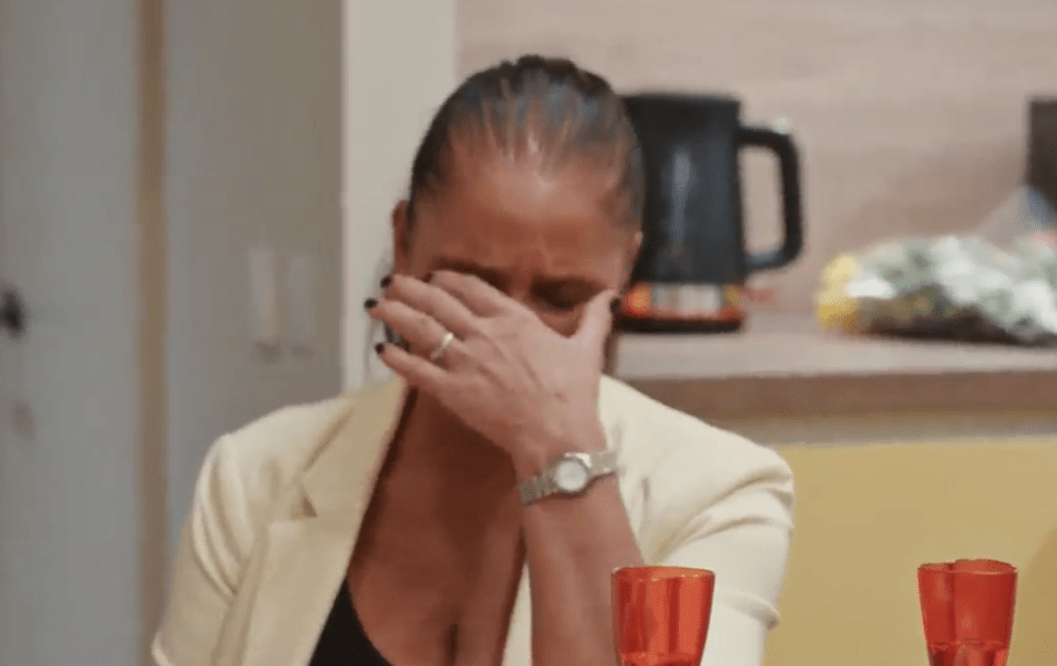 a woman is covering her face with her hand while sitting at a table .