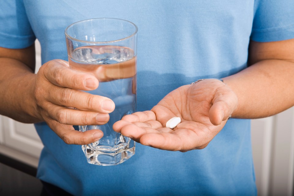 a man is holding a glass of water and a pill in his hand