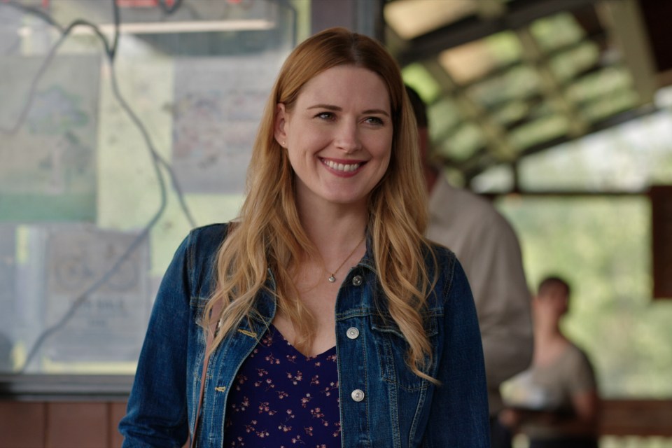 a woman wearing a denim jacket and a necklace smiles