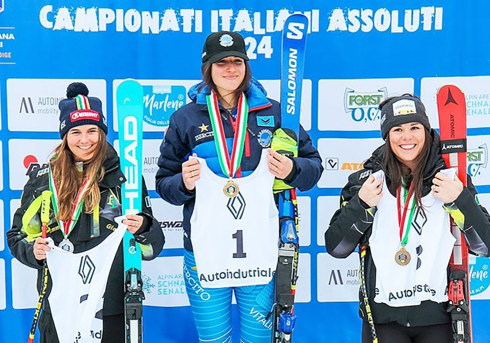 three female skiers stand on a podium holding their skis and medals