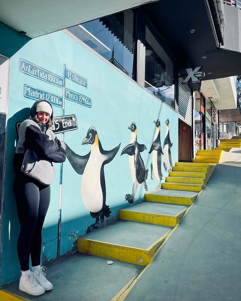 a woman stands in front of a painting of penguins on a wall