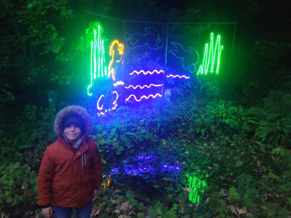 a boy in a red jacket stands in front of a neon sign