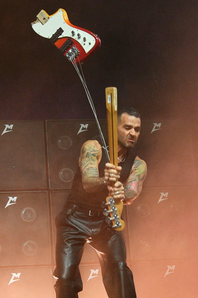 a man is playing a guitar in front of a wall with the letter m on it