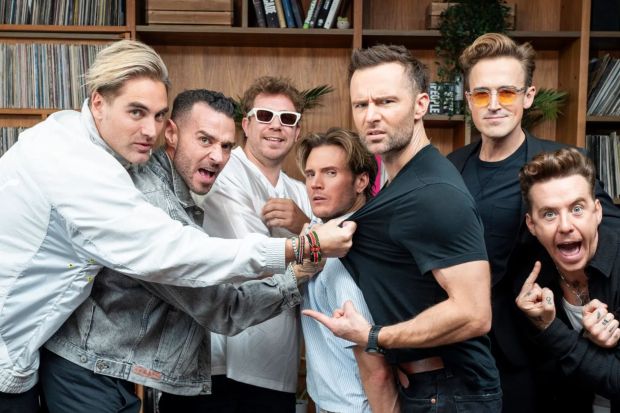 a group of men are posing for a picture and one of them is pointing at another man 's shirt