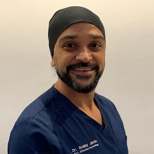 a man with a beard wears a black hat and a blue scrub top that says dr. bobby landu