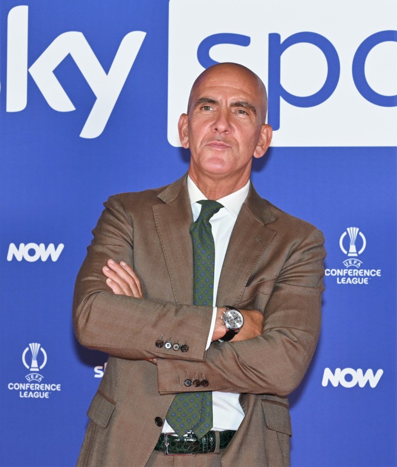 a man in a suit and tie stands in front of a blue background that says now