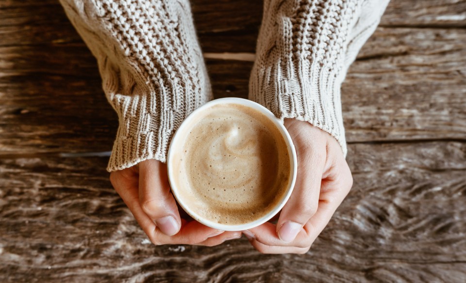 a person in a sweater is holding a cup of coffee