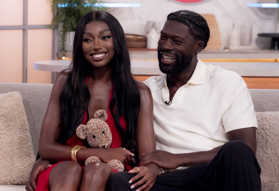 a man and a woman sit on a couch with a teddy bear