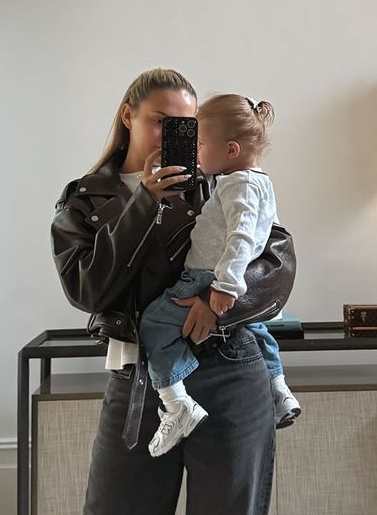 a woman is holding a baby and taking a selfie in the mirror .