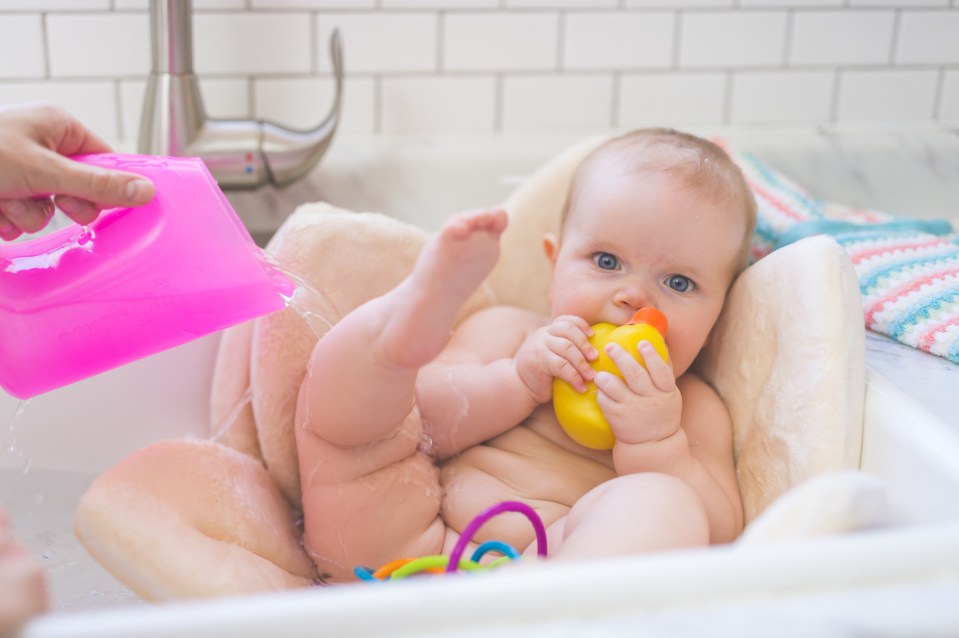 Mom gives her young infant daughter a bath in the sink