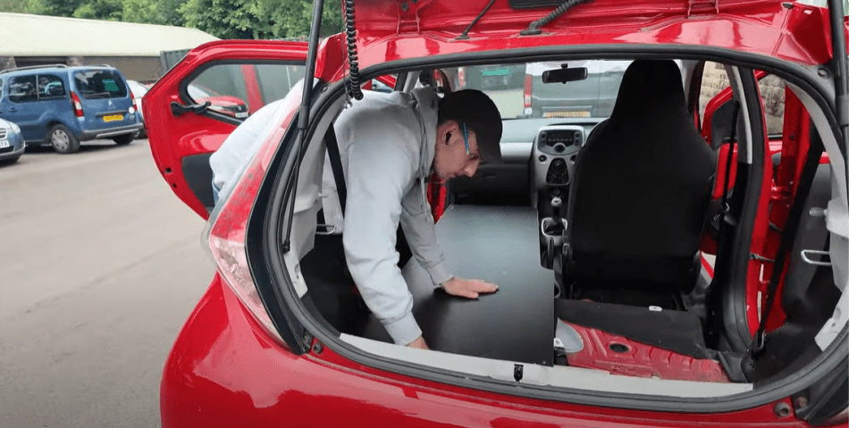 a man is looking into the back of a red car with a license plate that says ' yjc ' on it