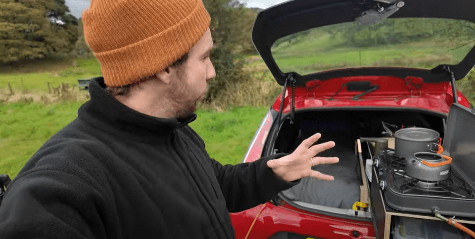 a man in an orange beanie is standing next to a red car