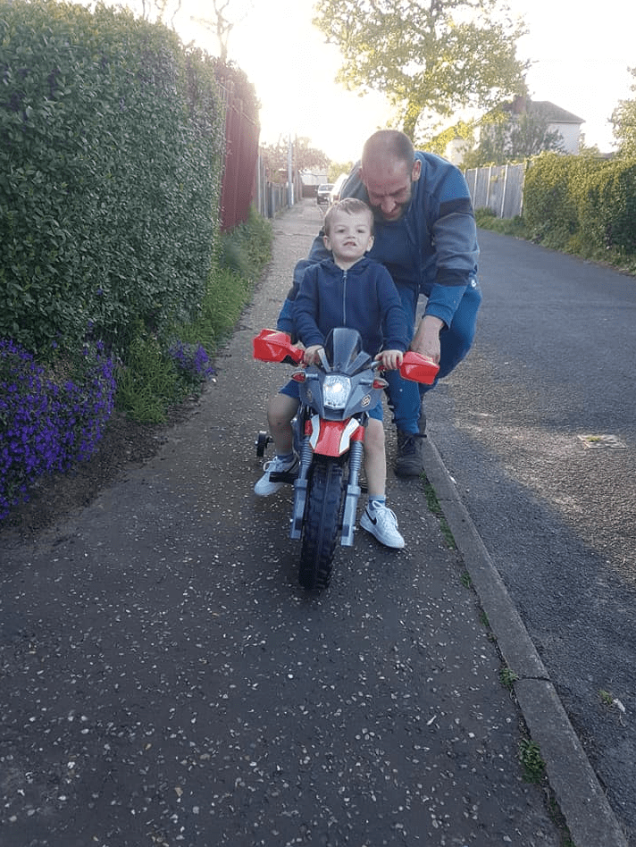 a man helps a little boy ride a toy motorcycle