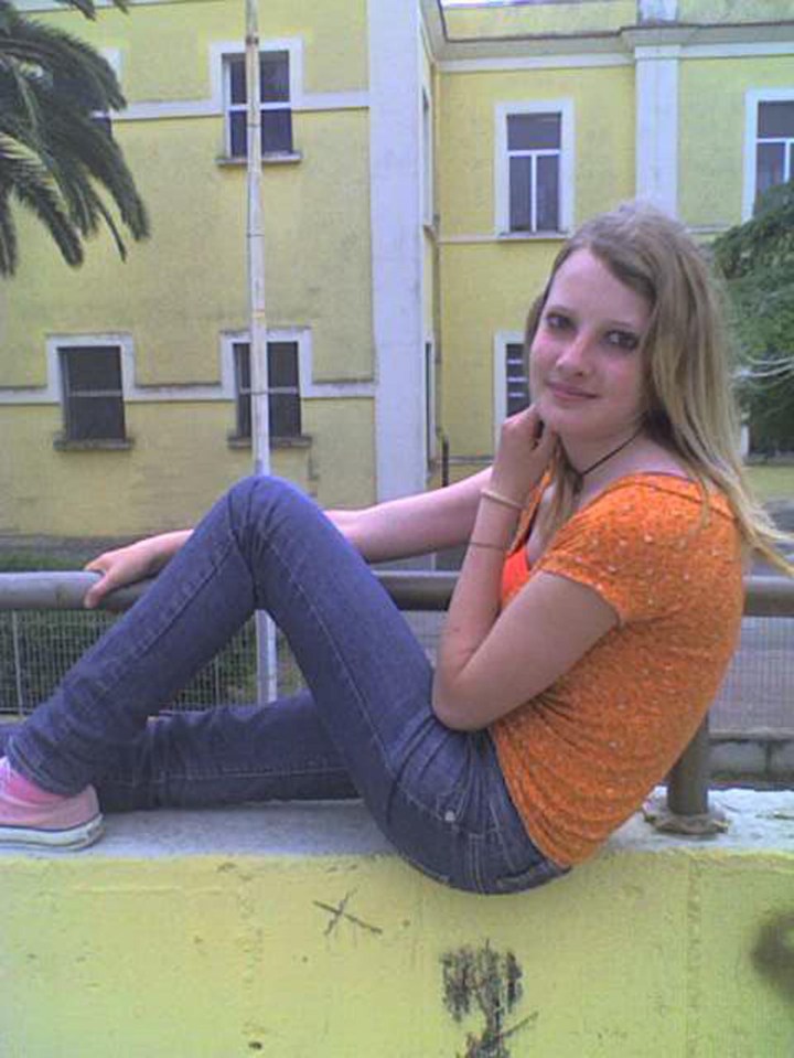 a girl sitting on a railing with a yellow building in the background