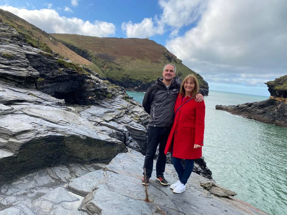 a man and woman standing on a rocky cliff overlooking the ocean